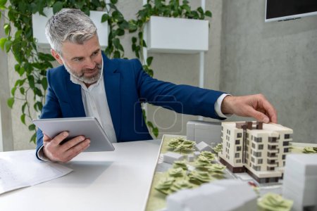 Téléchargez les photos : Architectes ou ingénieurs matures travaillant avec un modèle de plan et de maison au bureau, à l'aide d'une tablette numérique. - en image libre de droit