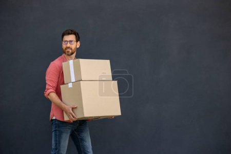 Photo for Carton boxes. Dark-haired young man in eyeglasses carrying carton boxes - Royalty Free Image