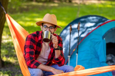 Photo for Enjoying nature. Smiling man with cup in hands enjoying nature in a hammock - Royalty Free Image
