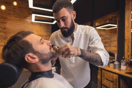 Photo for Attractive Caucasian man getting perfect shape of beard at barbershop. - Royalty Free Image