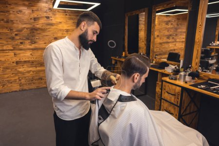 Téléchargez les photos : Homme salon de coiffure maître taillé cheveux client avec rasoir électrique au salon de coiffure. - en image libre de droit