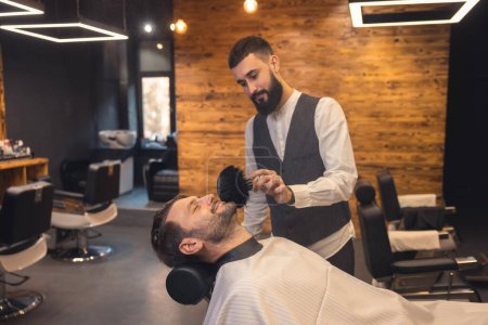 Téléchargez les photos : Attrayant caucasien homme obtenir parfait forme de barbe au salon de coiffure. - en image libre de droit
