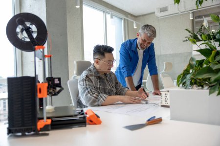 Téléchargez les photos : Ingénieurs expérimentaux hommes travaillant avec une imprimante 3D et un plan pour la conception de pièces mécaniques dans un atelier de haute technologie. - en image libre de droit