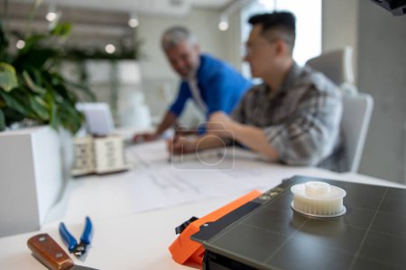 Téléchargez les photos : Équipe de deux architectes hommes utilisant une imprimante 3D dans un bureau et une maison en saillie, dessinant des plans. - en image libre de droit