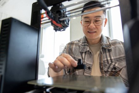 Foto de Hombre de ingeniería asiática diseñando piezas mecánicas usando impresora 3D en la oficina. - Imagen libre de derechos