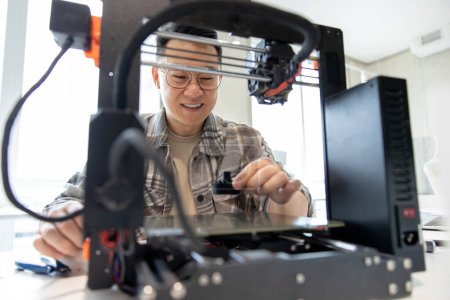 Foto de Hombre de ingeniería asiática diseñando piezas mecánicas usando impresora 3D en la oficina. - Imagen libre de derechos