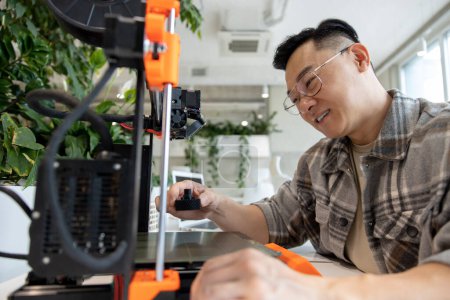 Téléchargez les photos : Asiatique ingénieur conception de pièces mécaniques à l'aide de l'imprimante 3D dans le bureau. - en image libre de droit
