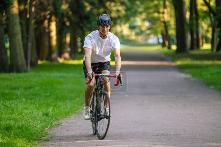 Photo for Healthy lifestyle. Young man in protective hemlet riding a bike in a park - Royalty Free Image