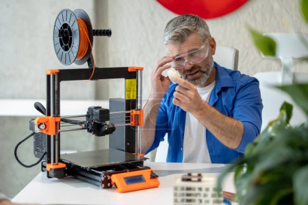 Téléchargez les photos : Impression de technicien mature en imprimante 3D, en utilisant une machine d'impression tridimensionnelle pour le travail. - en image libre de droit