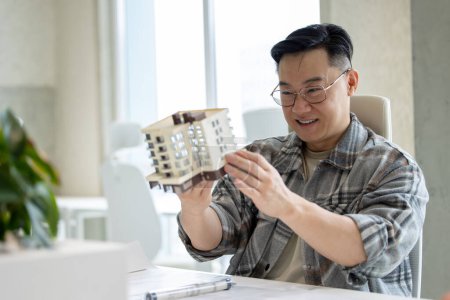 Foto de Hombre asiático con modelo de casa impreso con impresora 3D en la oficina de luz del laboratorio creativo. - Imagen libre de derechos