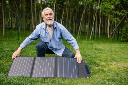 Photo for Gray haired senior man holding solar panel on in green yard. - Royalty Free Image
