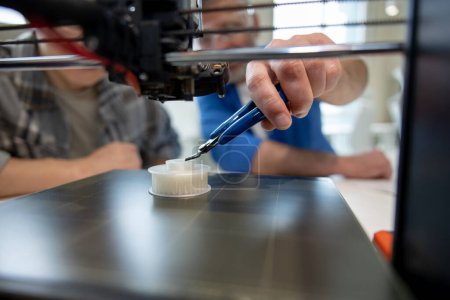 Téléchargez les photos : Designer méconnaissable travaillant avec l'imprimante 3D laboratoire créatif. - en image libre de droit