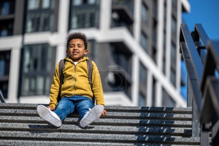 Photo for Resting. Cute schoolboy sitting on the steps and resting - Royalty Free Image