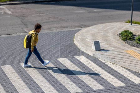 Photo for On a crosswalk. Schoolboy with backpack on his back crossing the street - Royalty Free Image