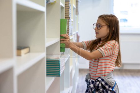 Photo for Schoolgirl. Long-haired girl in eyeglasses putting a book on the shelf - Royalty Free Image