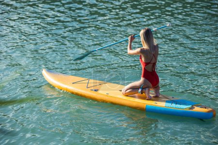 Photo for Beautiful blonde woman paddling on sup board in blue ocean. - Royalty Free Image