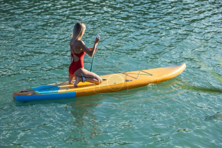 Foto de Hermosa mujer rubia remando en sup board en el océano azul. - Imagen libre de derechos