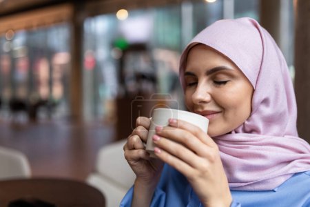 Téléchargez les photos : Café savoureux. Femme en hijab rose buvant du café et souriant - en image libre de droit