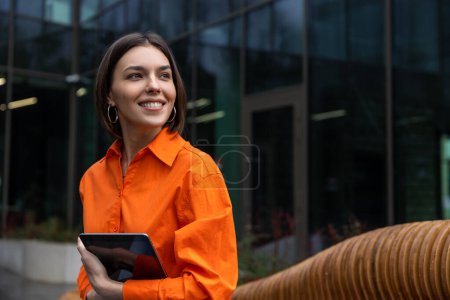 Téléchargez les photos : Nomade de Digitall. Fille souriante en chemise orange avec un appareil qui a l'air satisfait - en image libre de droit