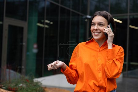 Photo for On the call. Girl in orange shirt talking on the phone and smiling - Royalty Free Image