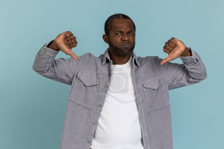 Photo for Sad black man wearing gray shirt showing dislike gesture standing isolated over blue background - Royalty Free Image
