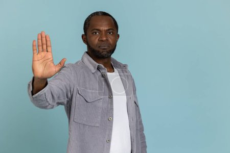 Photo for Serious black man wearing gray shirt showing stop sign standing isolated over blue background - Royalty Free Image