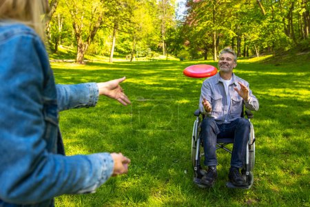 Photo for Playing frisbee. Man on a wheelchair and his wife playing frisbee and loking contented - Royalty Free Image