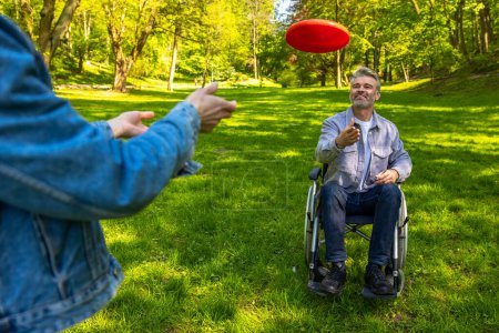 Photo for Playing frisbee. Man on a wheelchair and his wife playing frisbee and loking contented - Royalty Free Image
