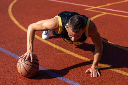 Photo for Handsome young man doing push ups with a basketball ball workout outdoor on basketball court. - Royalty Free Image
