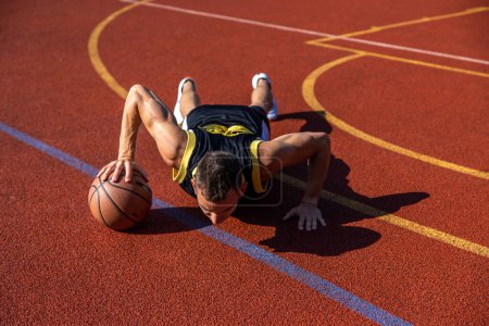 Téléchargez les photos : Jeune homme sportif faisant des pompes avec une balle de basket-ball sur le terrain de basket-ball. - en image libre de droit