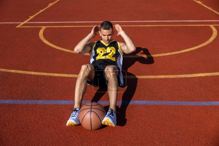 Photo for Attractive man doing crunches has workout outdoor on basketball court. - Royalty Free Image