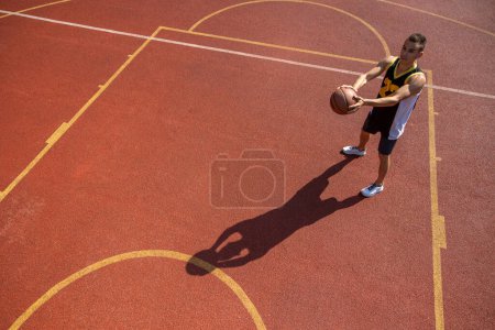 Foto de Atlético deportista masculino jugando baloncesto lanzando pelota en el patio de recreo, espacio de copia. - Imagen libre de derechos