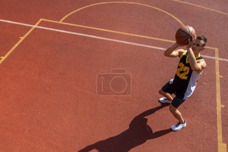 Foto de Atlético deportista masculino jugando baloncesto lanzando pelota en el patio de recreo, espacio de copia. - Imagen libre de derechos