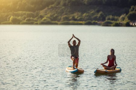 Téléchargez les photos : Paddle sup board surfeurs femme et homme au coucher du soleil pratiquant le yoga. - en image libre de droit