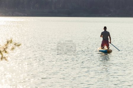 Téléchargez les photos : Silhouette homme sur le supboard au milieu du lac au coucher du soleil. - en image libre de droit