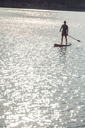 Foto de Silueta de hombre en el supboard en el medio del lago al atardecer. - Imagen libre de derechos