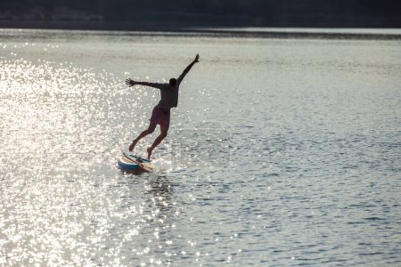 Foto de Hombre silueta salto de supboard en el agua. - Imagen libre de derechos