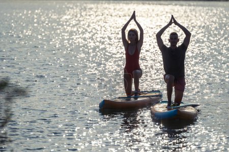 Téléchargez les photos : Surfeurs femme et homme pratiquant le yoga sur supboard et méditant ensemble. - en image libre de droit