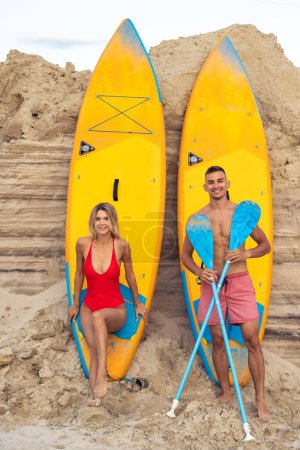 Photo for Attractive Caucasian couple man and woman with sup boards on sandy beach. - Royalty Free Image