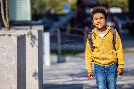 Téléchargez les photos : Un écolier dans la rue. écolier aux cheveux bouclés avec un sac à dos marchant dans la rue - en image libre de droit