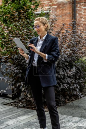 Téléchargez les photos : Une femme occupée. Mignon jeune manager en veste et pantalon avec une tablette à l'air occupé - en image libre de droit