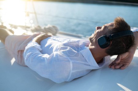 Téléchargez les photos : Détendez-vous. Homme en casque naviguant sur un yacht et l'air détendu - en image libre de droit