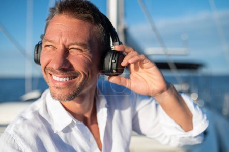 Foto de En un yate. Hombre feliz con auriculares escuchando música mientras navega en un yate - Imagen libre de derechos