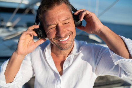 Téléchargez les photos : Heureux et détendu. Homme souriant dans un casque naviguant sur un yacht et l'air détendu - en image libre de droit