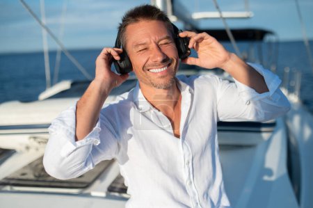 Photo for Happy and relaxed. Smiling man in headphones sailing n a yacht and looking relaxed - Royalty Free Image