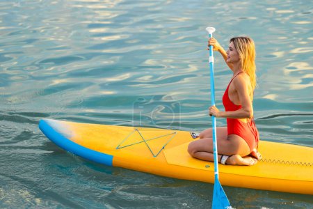 Téléchargez les photos : Mode de vie sain, sports nautiques. Fille avec pagaie sur sous-bord flottant sur l'eau dans l'océan. - en image libre de droit