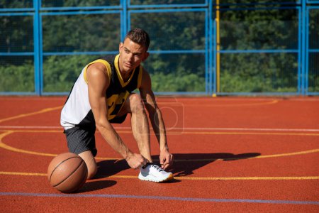 Photo for Adult athletic sporty man standing on basketball court ties his shoelaces before playing game. - Royalty Free Image