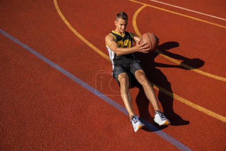 Foto de Atlético joven haciendo sentadas y abdominales ejercitando los músculos abdominales al aire libre en la cancha de baloncesto. - Imagen libre de derechos