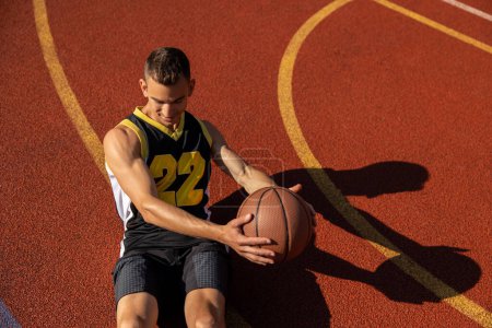 Photo for Athletic young man doing sit ups and crunches exercising abdominal muscles outdoor on basketball court. - Royalty Free Image