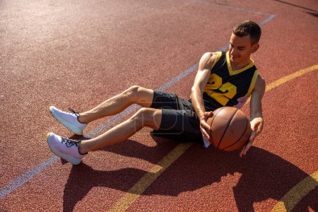 Photo for Sporty strong man doing abs workout with ball outdoor on basketball court. - Royalty Free Image